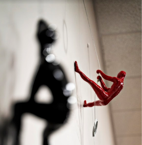 miniature sculpture of a red man climbing a wall 