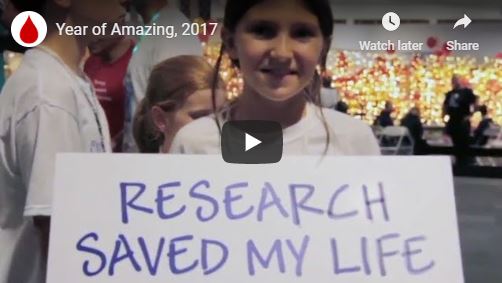 still shot from video: girl holding a poster that says Research saved my life